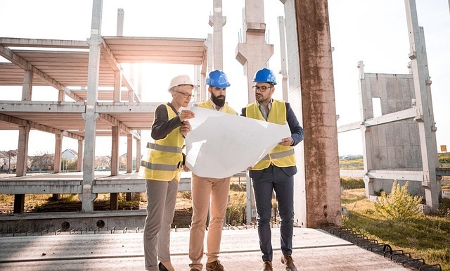 Three construction supervisors look at a plan in front of an unfinished building.